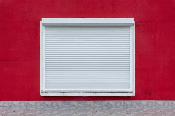 Persiana enrollable blanca cerrada sobre una ventana de pared roja, el tipo de avería que atendemos en Pamplona Persiana enrollable blanca cerrada sobre una ventana de pared roja, el tipo de avería que atendemos en Pamplona